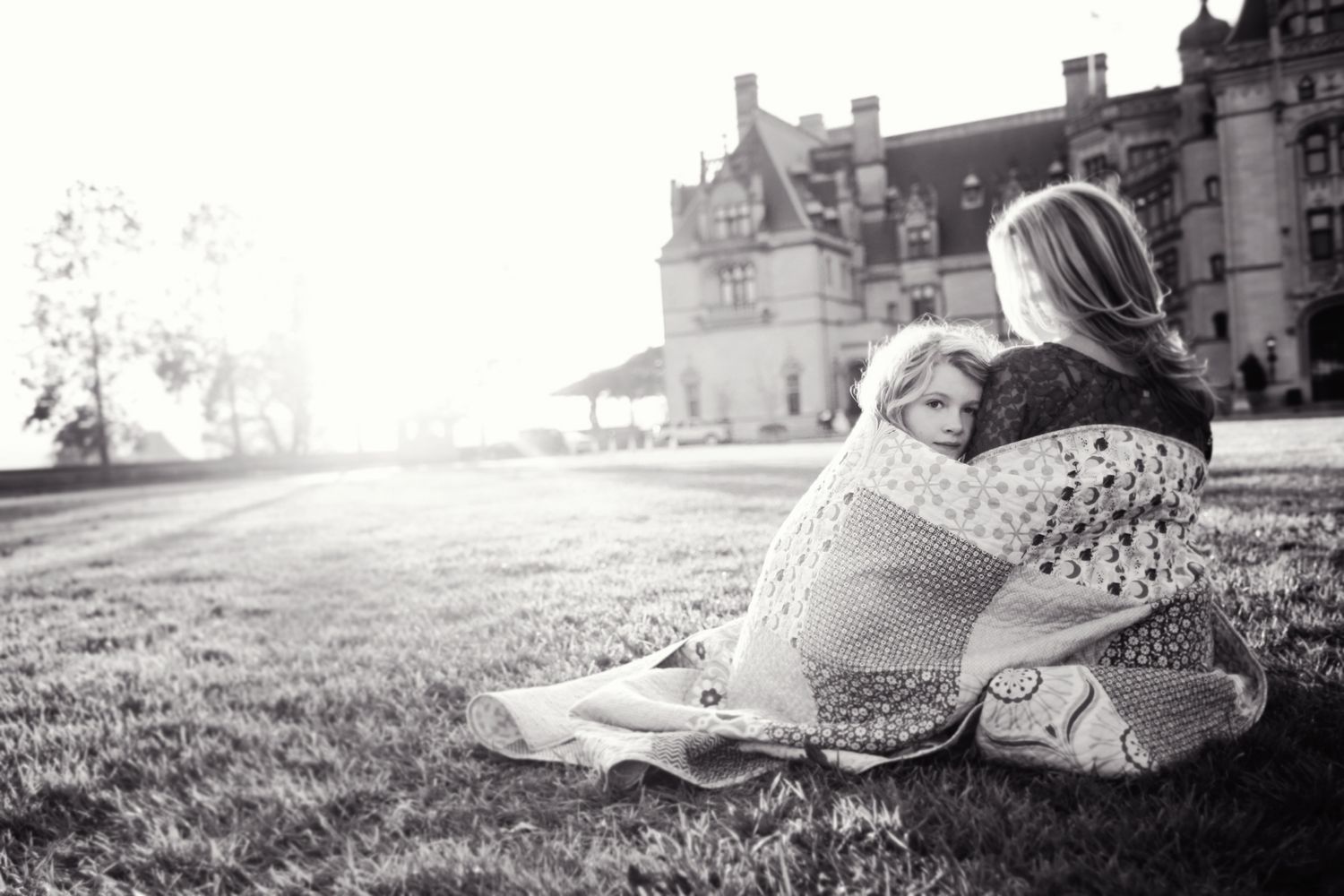 Black and white photo of two people relaxing on grass with castle in background.