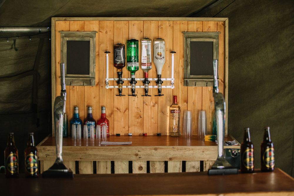 Rustic wooden bar display with mounted liquor bottles and glasses on shelving.