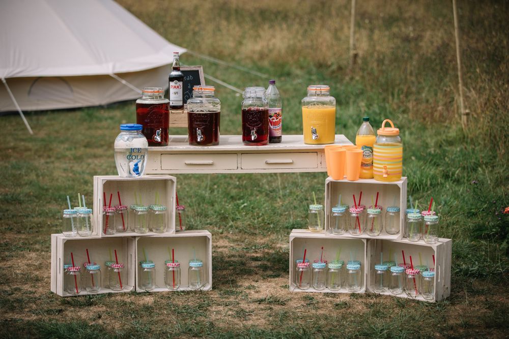 Outdoor drink station with wooden crates displaying glassware and beverage dispensers.