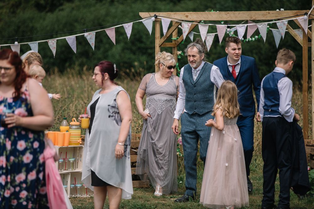 Wedding guests gather under bunting at an outdoor reception with drinks.