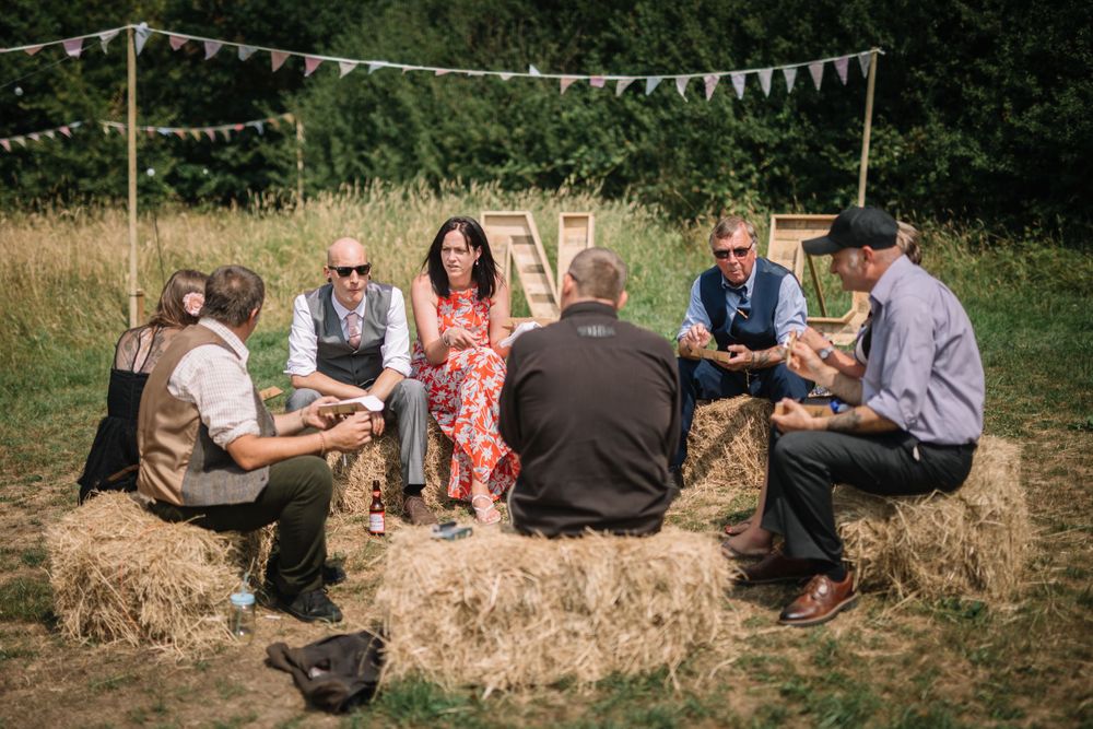 Wedding guests sitting on hay bales during outdoor reception gathering.
