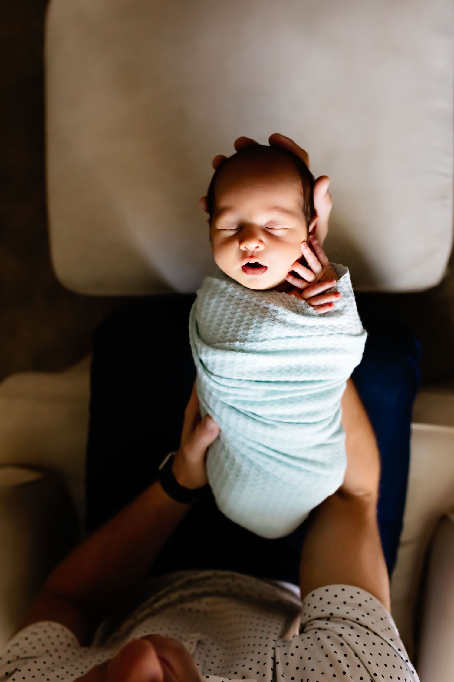 A sleeping newborn swaddled in mint green fabric lies peacefully on a dark surface.
