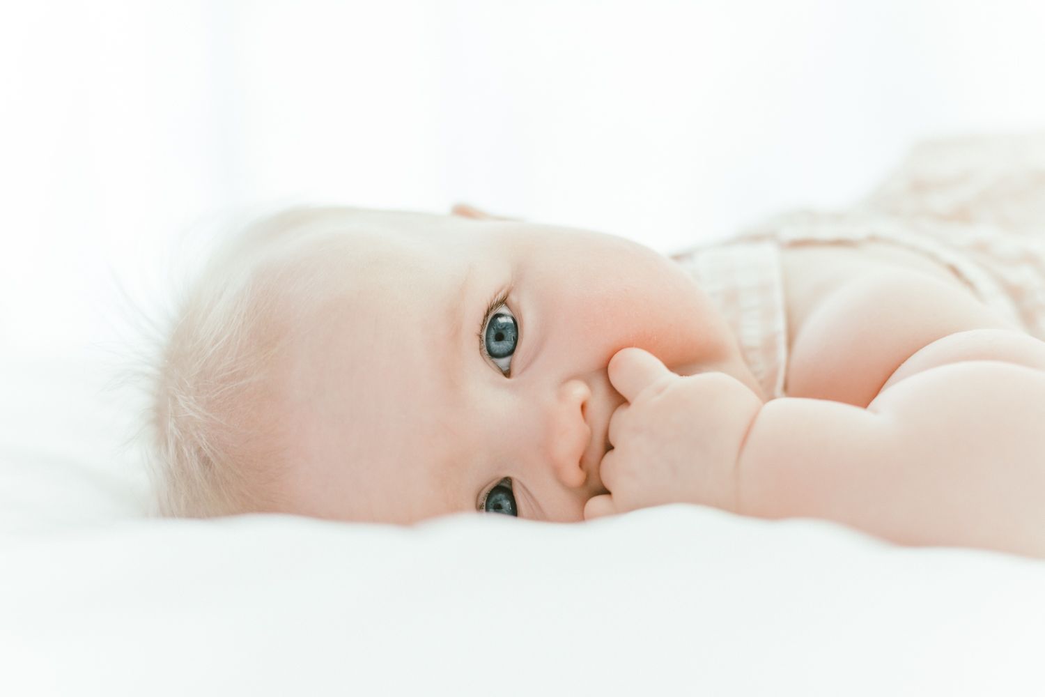 Close-up portrait of baby with bright eyes lying on white bedding.