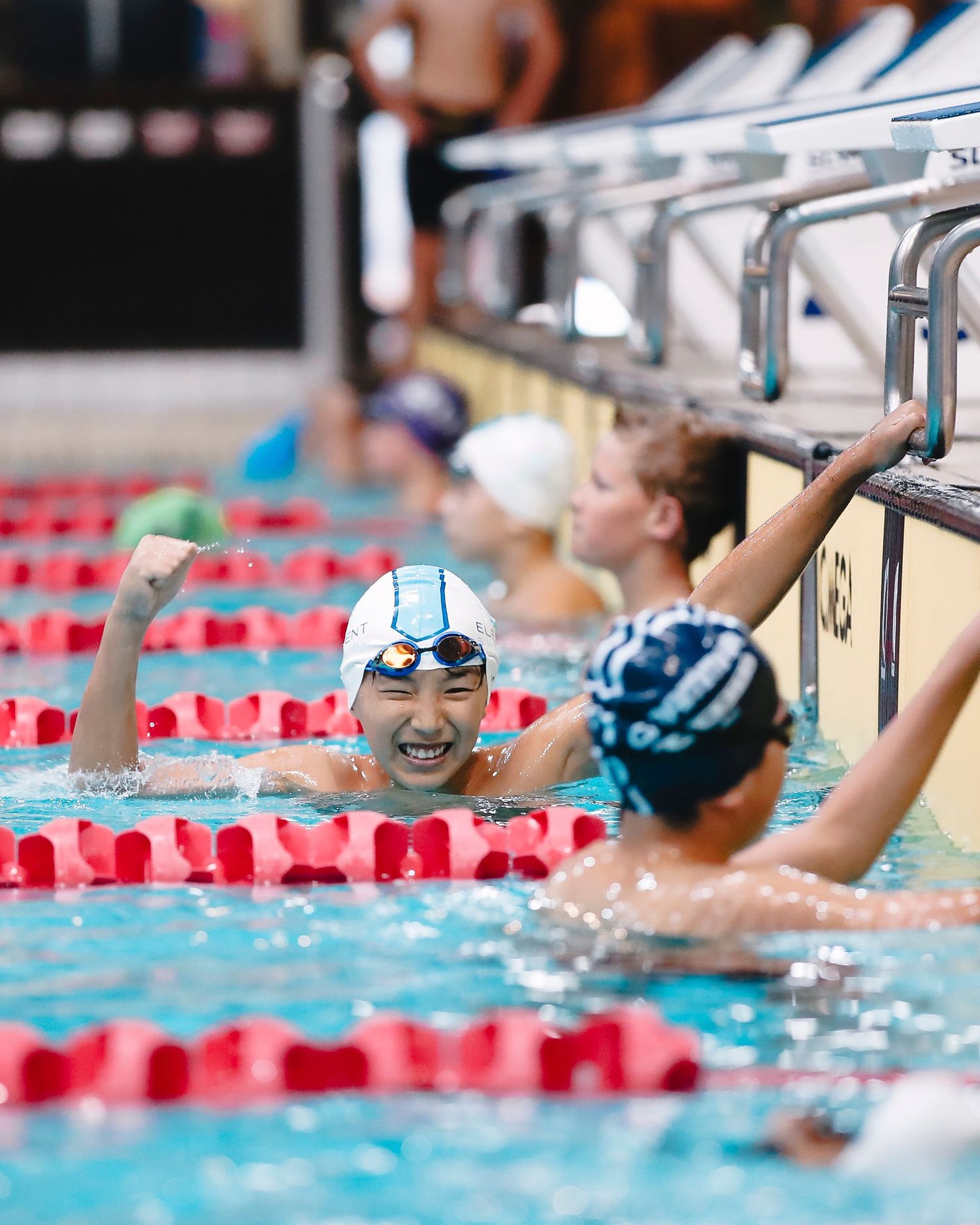 Swimmers at pool edge during competitive swimming meet with lane dividers.