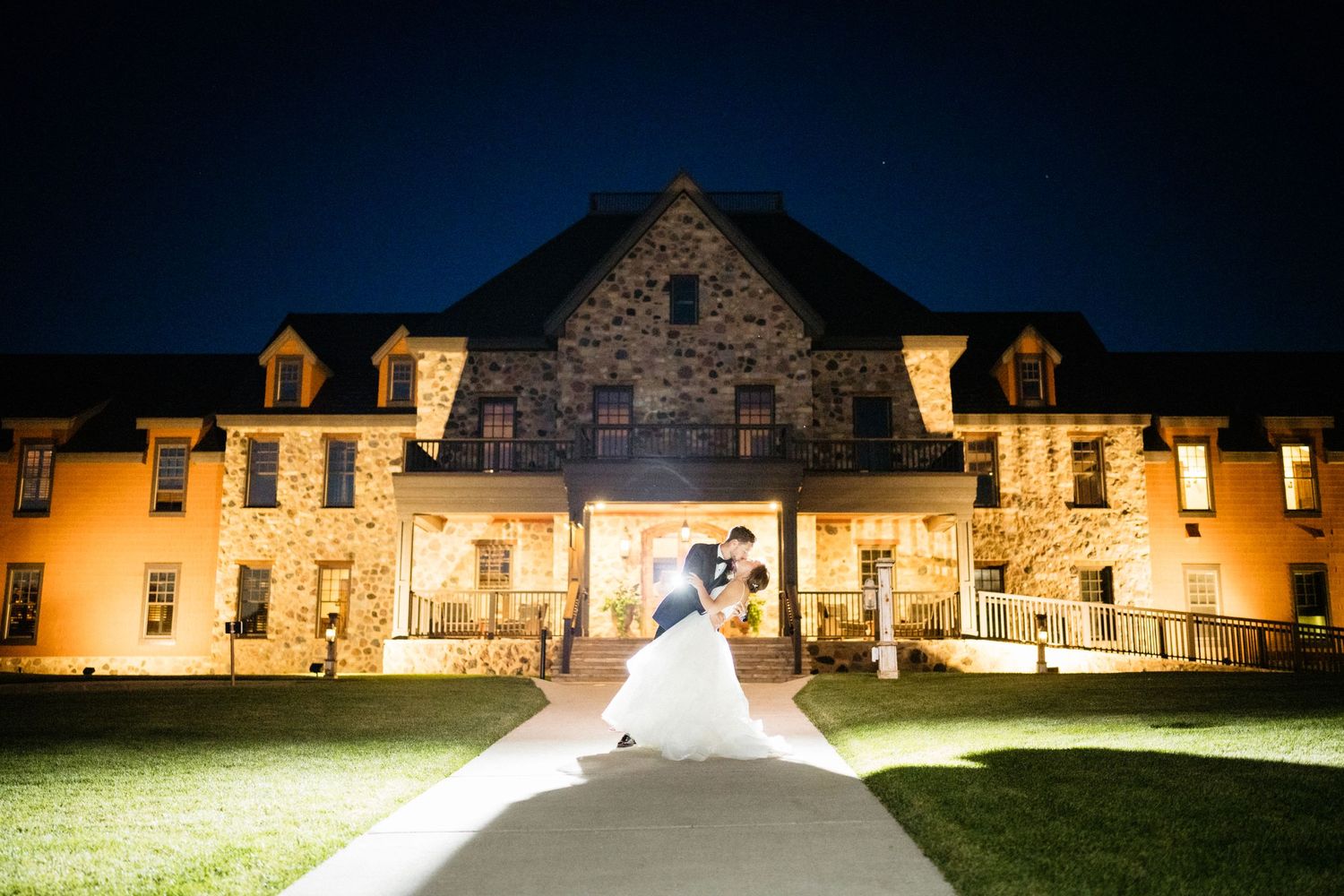 Illuminated stone mansion glows warmly against dark blue evening sky during wedding celebration.