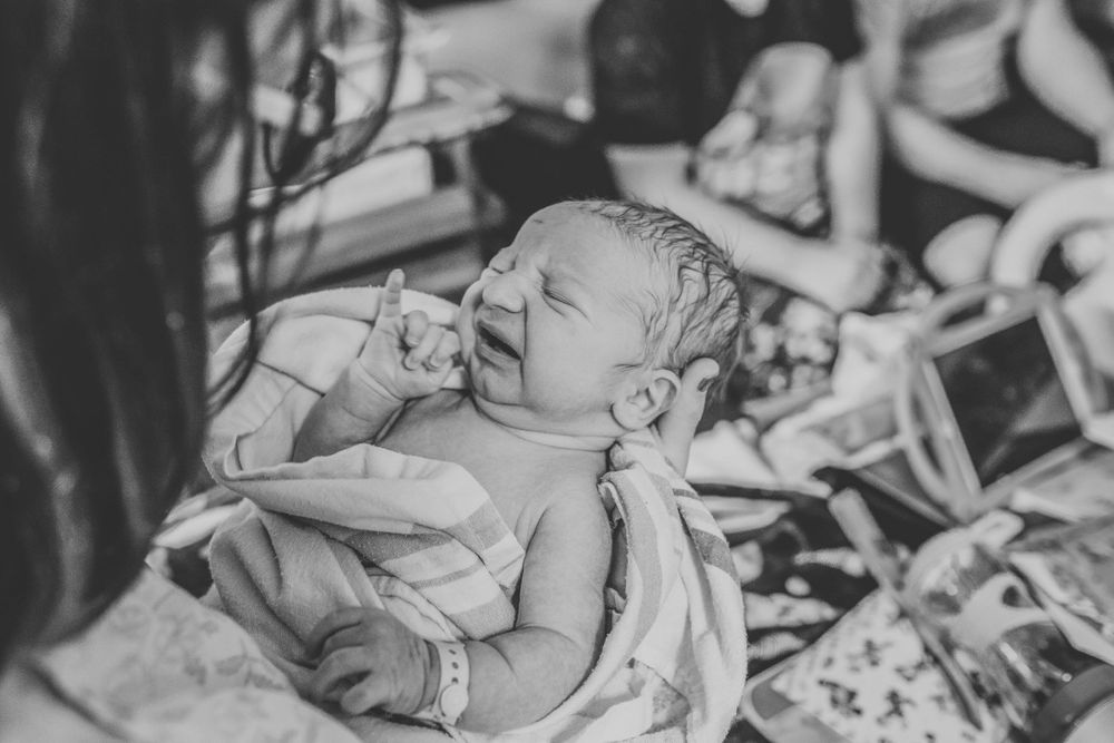 Crying newborn baby being held in hospital blanket moments after birth.