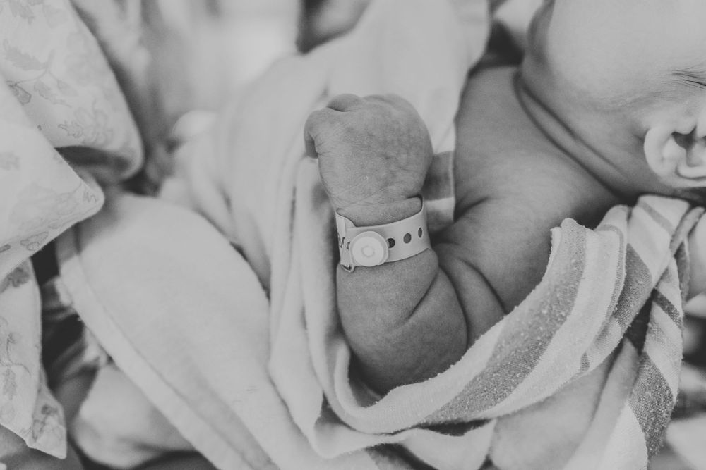 Close-up of newborn baby hand with hospital ID bracelet wrapped in soft blanket.