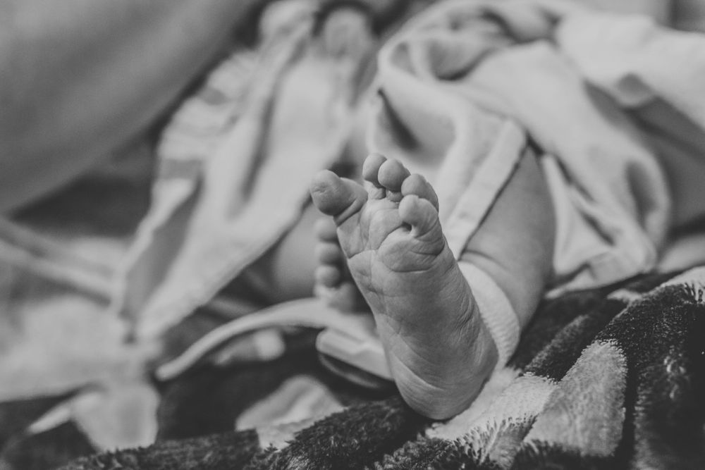 Tiny newborn baby feet resting on soft blanket in hospital after birth.