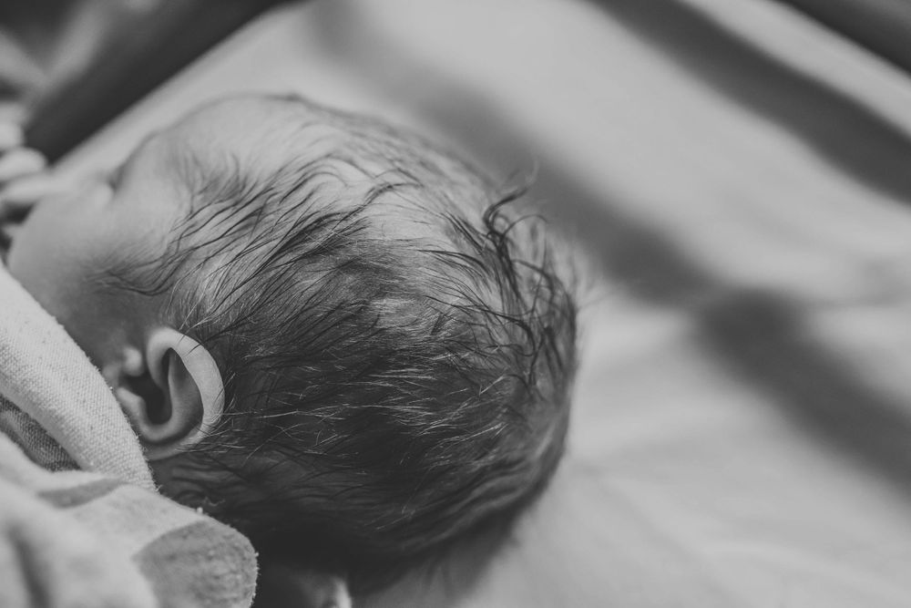 Close-up of newborn baby head with dark hair resting on hospital blanket.