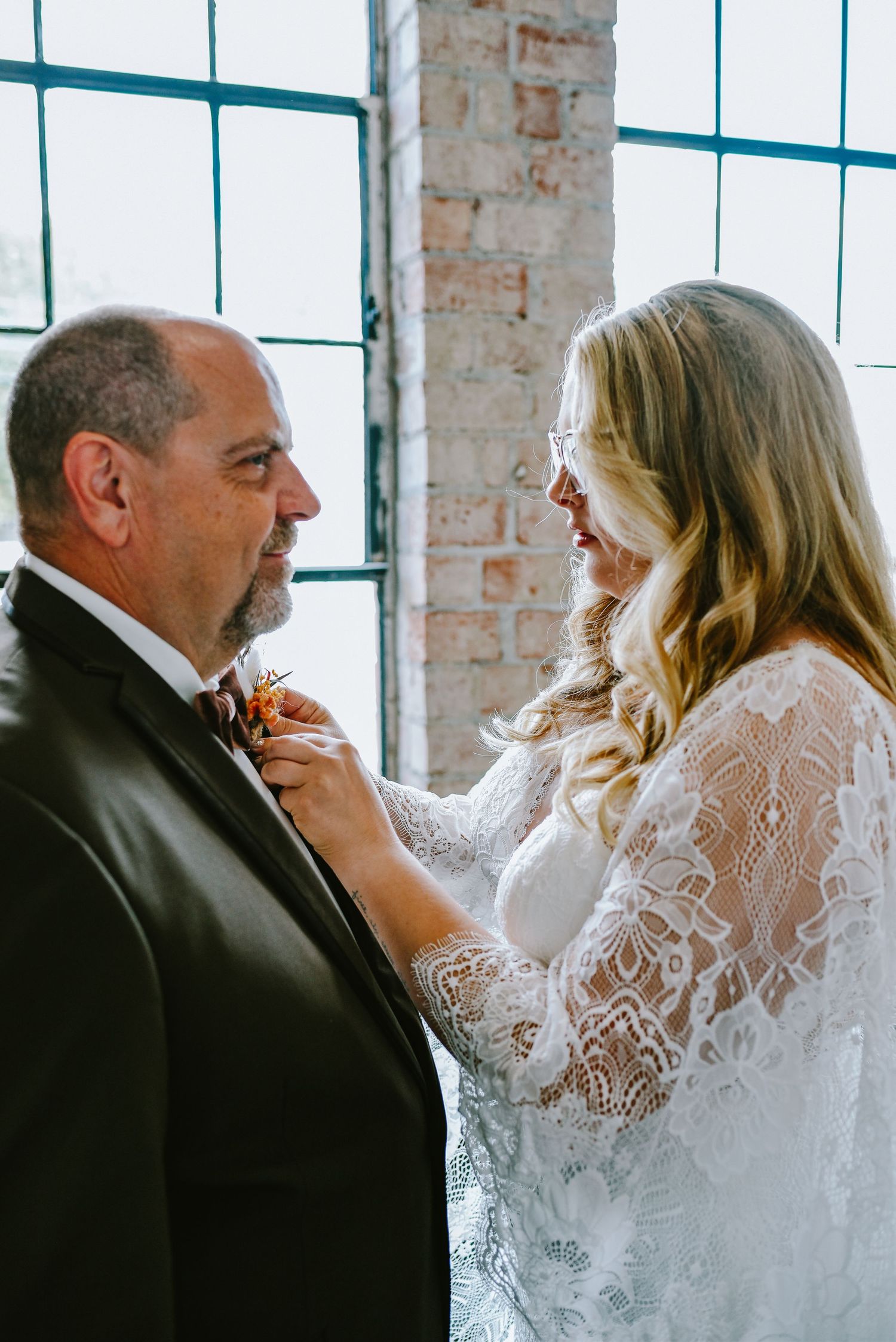 An intimate moment shared between two people in formal wear by a window with exposed brick.