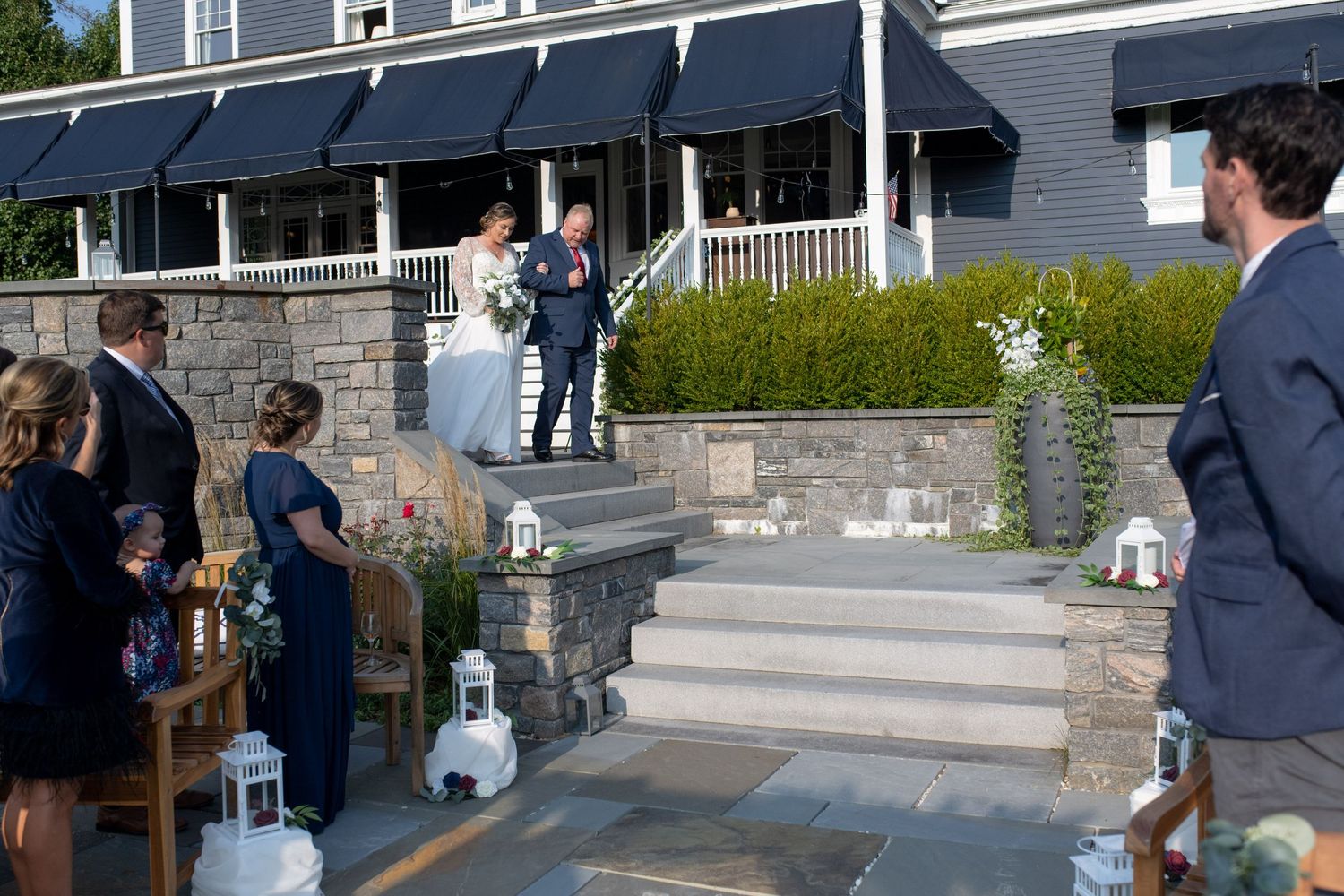 Outdoor wedding ceremony setup with white lanterns lining stone steps and black awnings in the background.