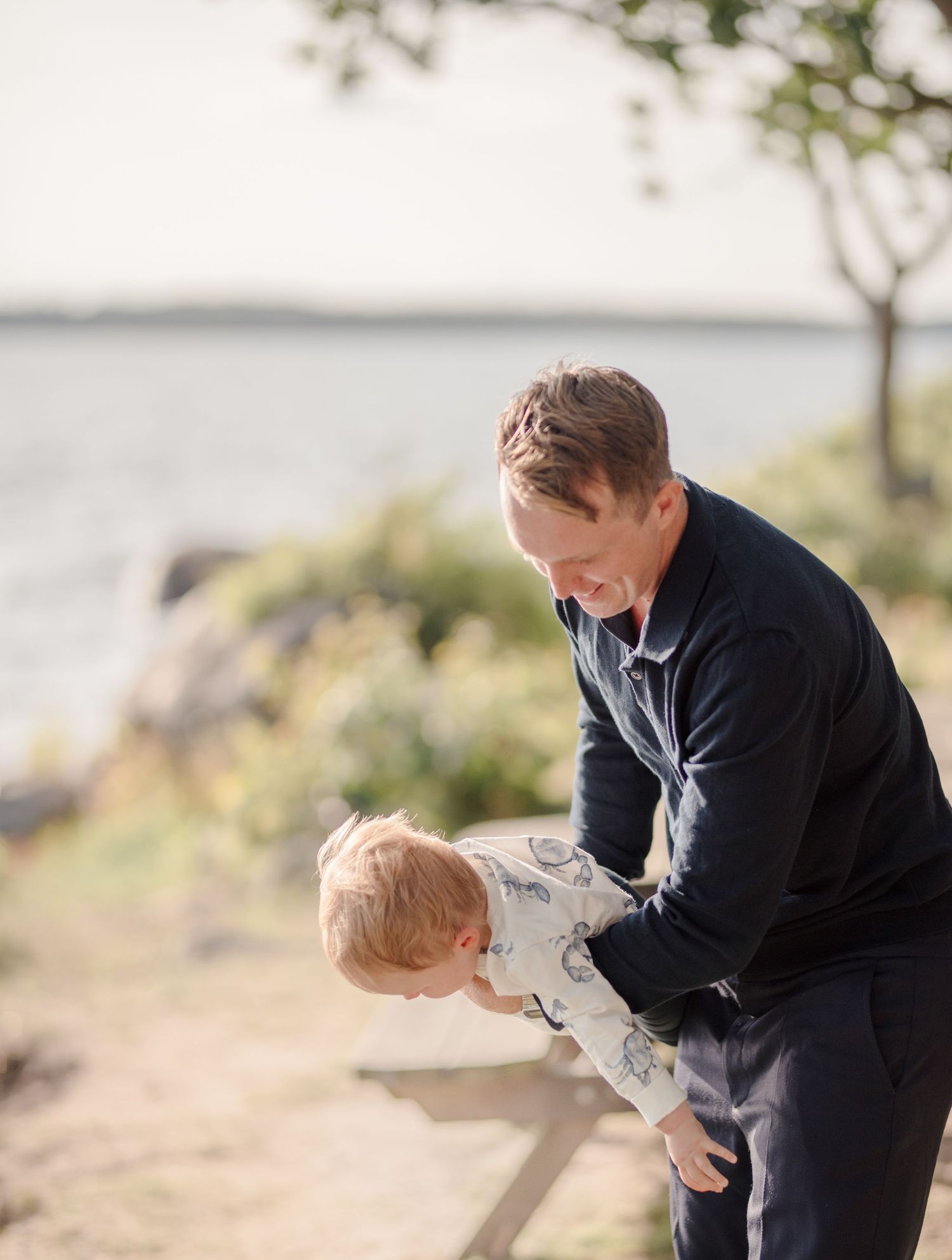 Parent and toddler playing together by the waterfront on a sunny day.