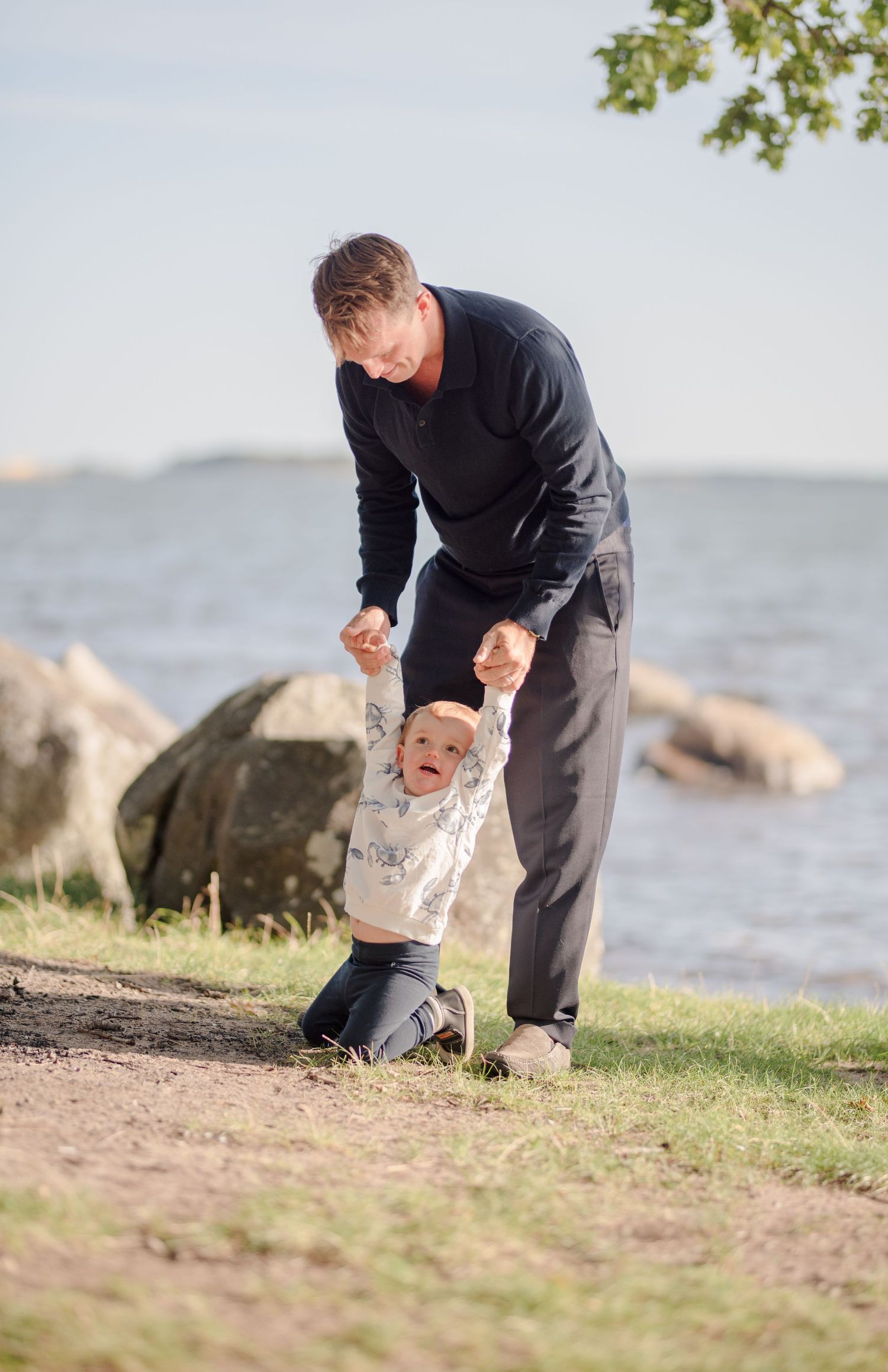 Adult and child playing together on grassy area by rocky shoreline.