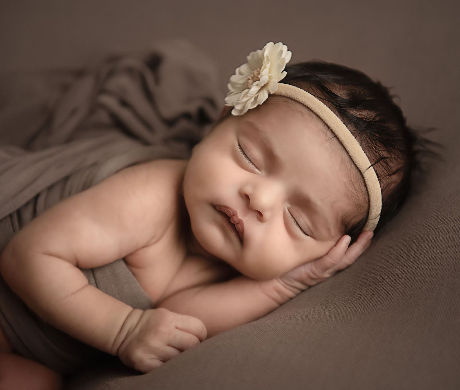 Sleeping newborn wearing floral headband during professional portrait session.