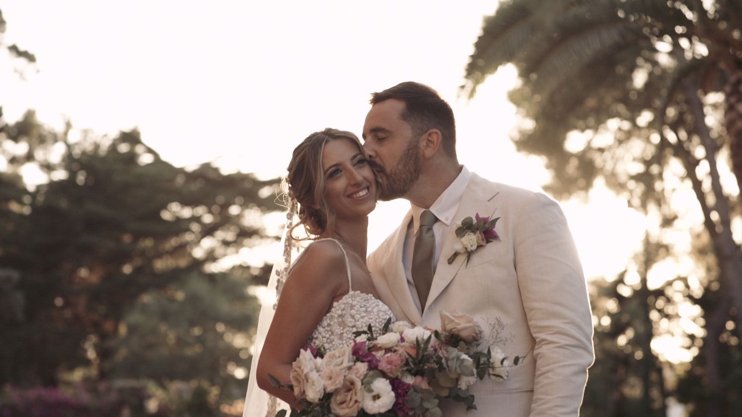 Sunset wedding portrait of couple sharing intimate moment with bouquet and formal attire.