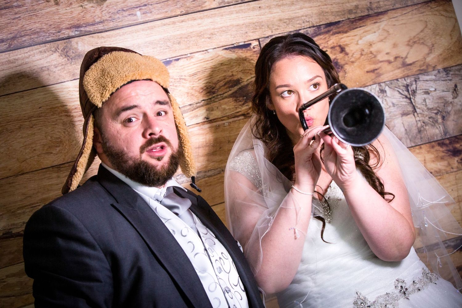 A playful wedding photo with a camera and fun expressions against a rustic wood backdrop.