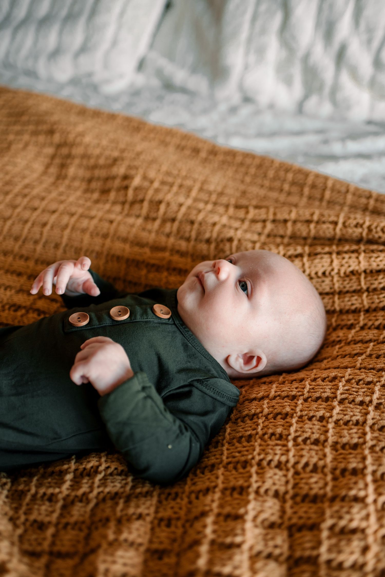 Infant wearing dark outfit lying on textured brown knit blanket.