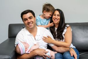 Portrait of mom and dad with toddler son and newborn infant smiling on sofa - shot by Milwaukee family photographer Rachel Dickman.