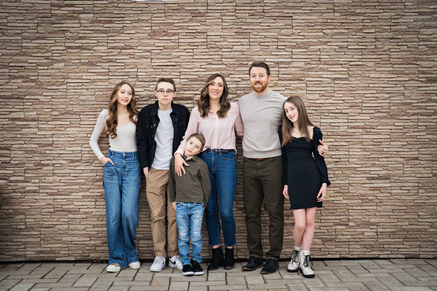 Family of 6 smiling against brick wall, family portrait shot by Milwaukee family photographer Rachel Dickman