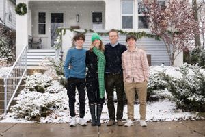 Portrait of family of 4 smiling, standing outside their house on a snowy day - shot by Milwaukee family photographer Rachel Dickman