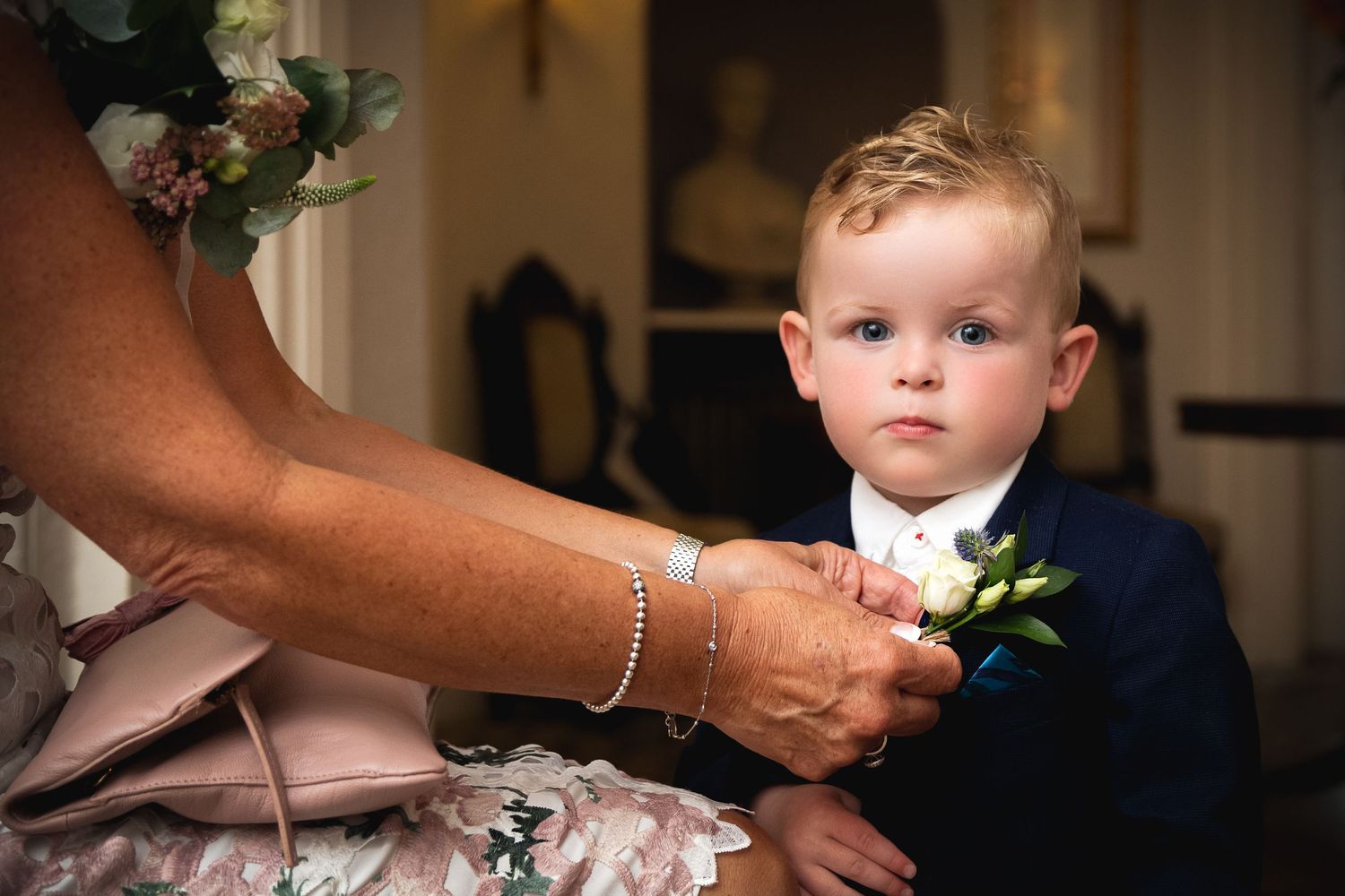 Small child in formal wear having boutonniere pinned on navy suit jacket.