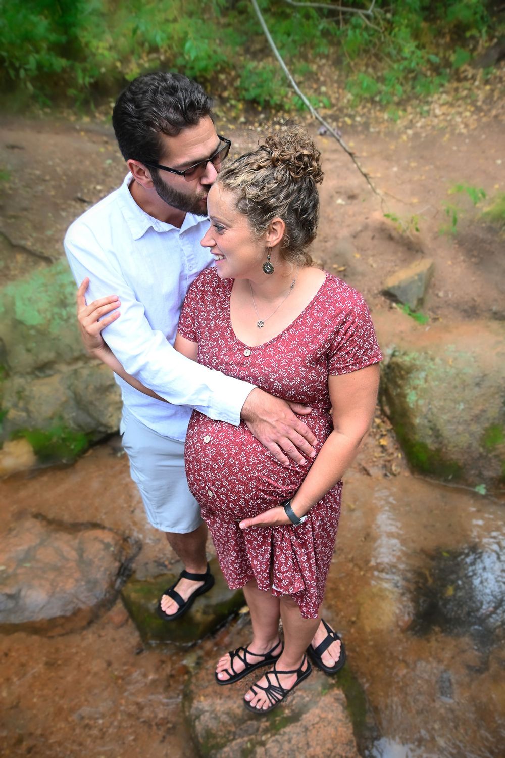 Couple standing in creek bed surrounded by lush green foliage.
