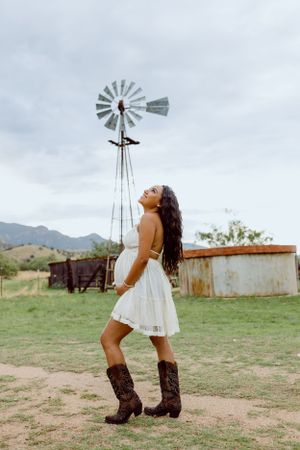 Cowboy boots and white dress against a rustic windmill backdrop.