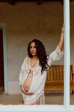 A white crochet fringe cover-up is worn in front of a rustic porch setting.