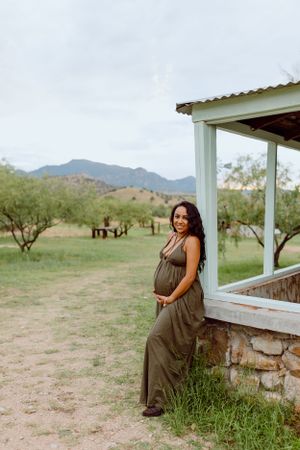 A stone foundation ranch house with white posts overlooks a grassy field with mountains in the distance.