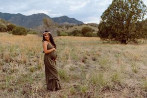 Maternity photoshoot in a desert landscape with mountains and brush in the background.