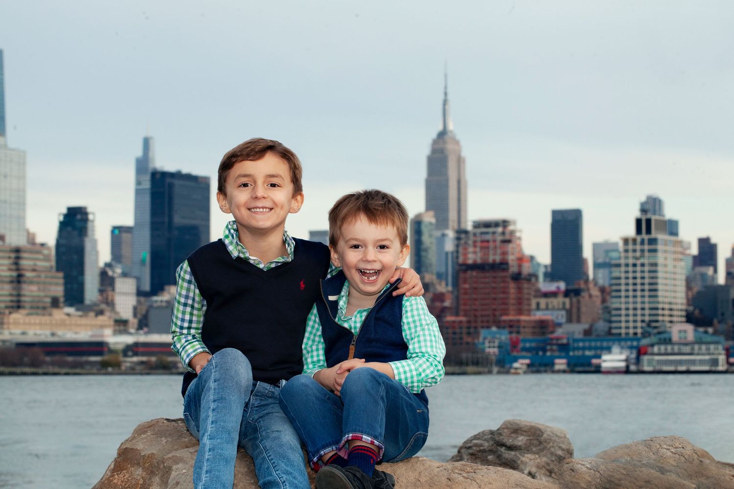 Two children sitting on rocks by the water with Manhattan skyline behind them.