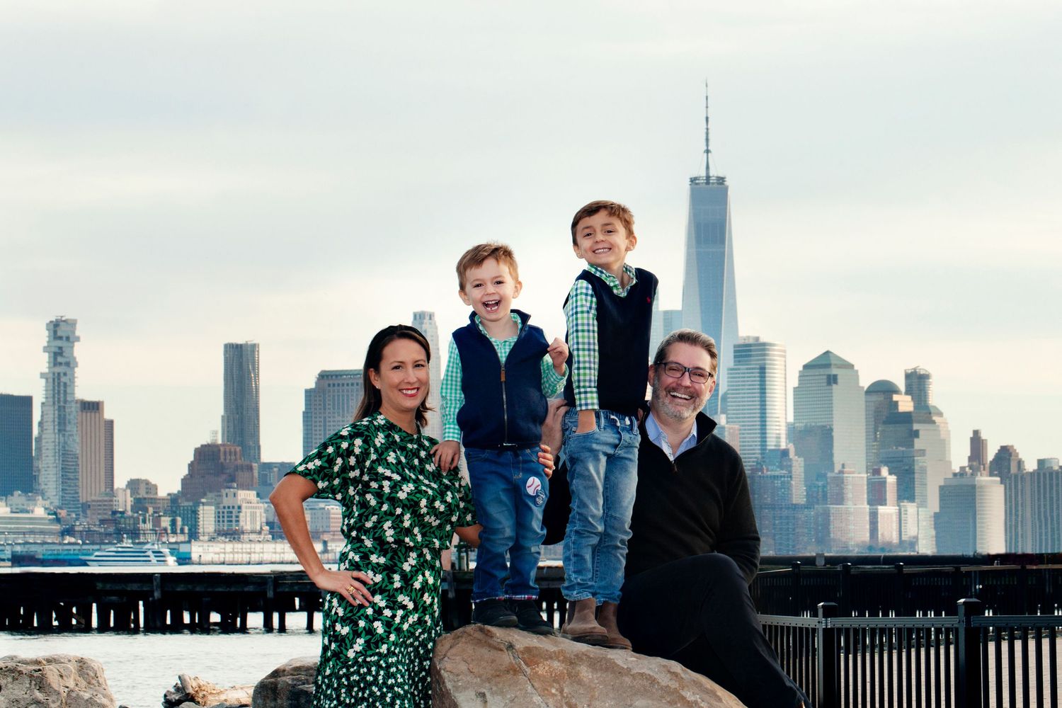 Family gathered on rocks with Manhattan skyline backdrop.