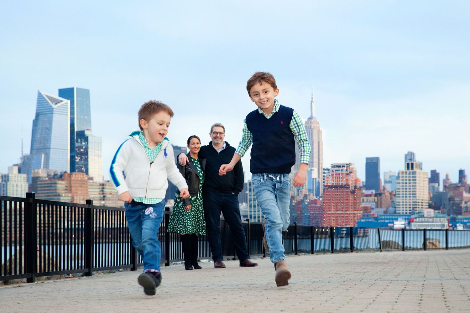 Children running along waterfront path with NYC skyline in background.