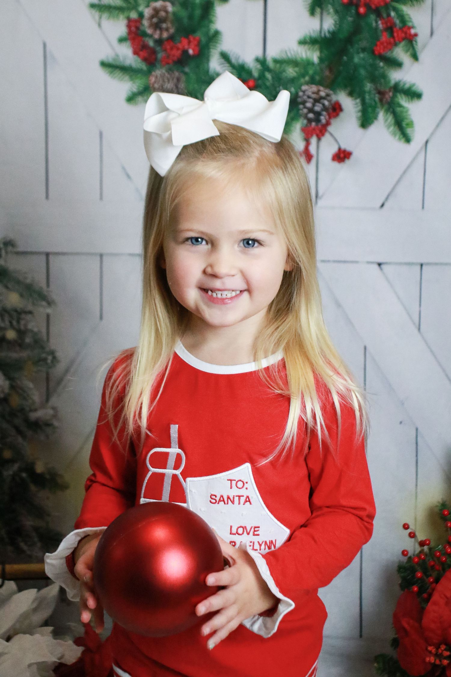 Christmas themed portrait with red sweater, white bow and large ornament against white backdrop.