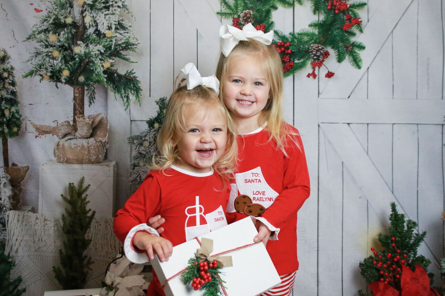 Christmas themed photo setup with siblings in matching red sweaters and holiday decorations.