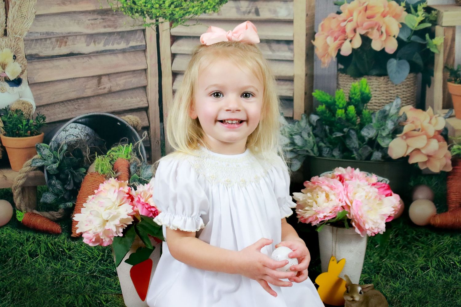Garden themed photo setup with pink flowers and greenery against wooden fence backdrop.