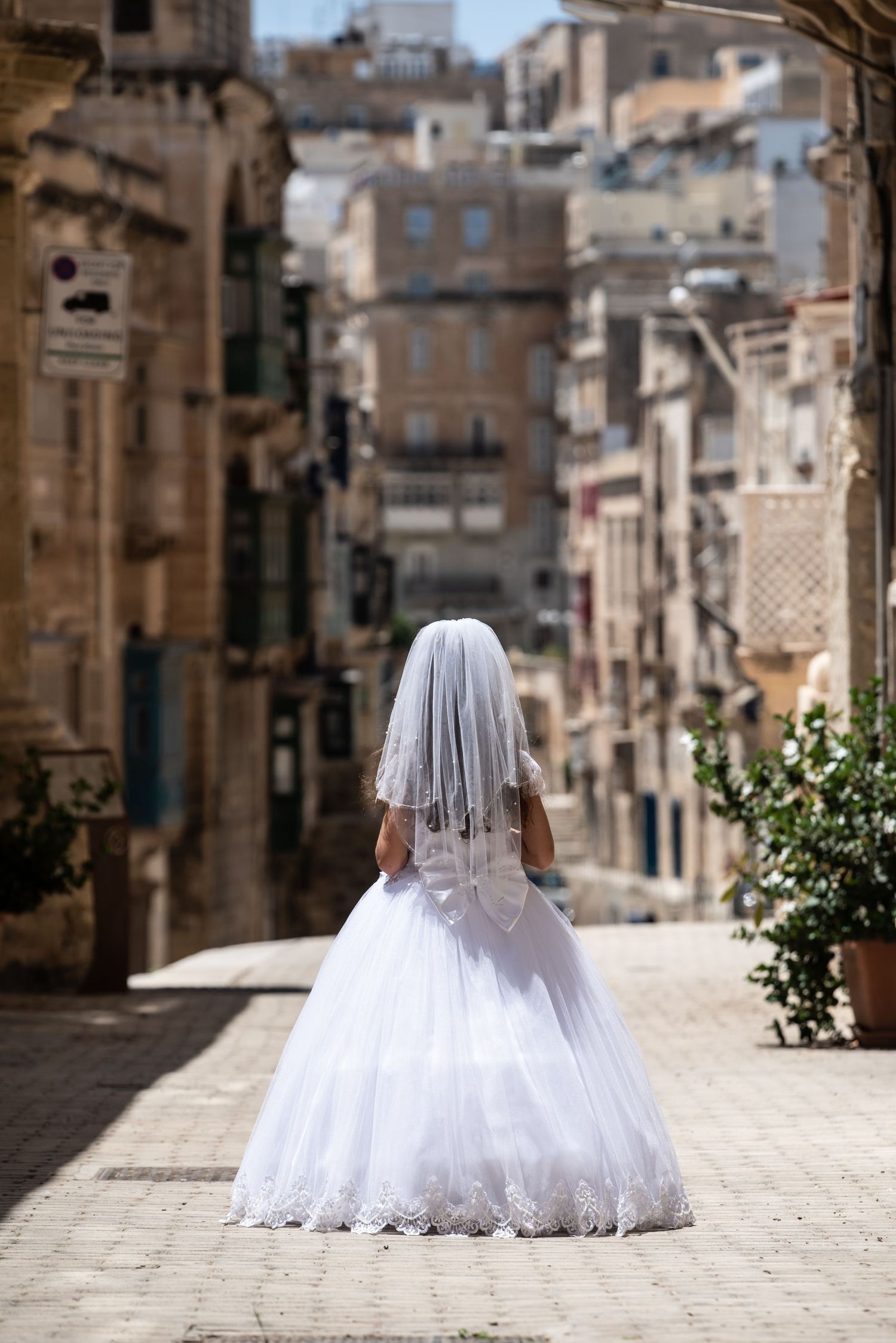 A white ballgown with veil photographed from behind on a historic stone street.