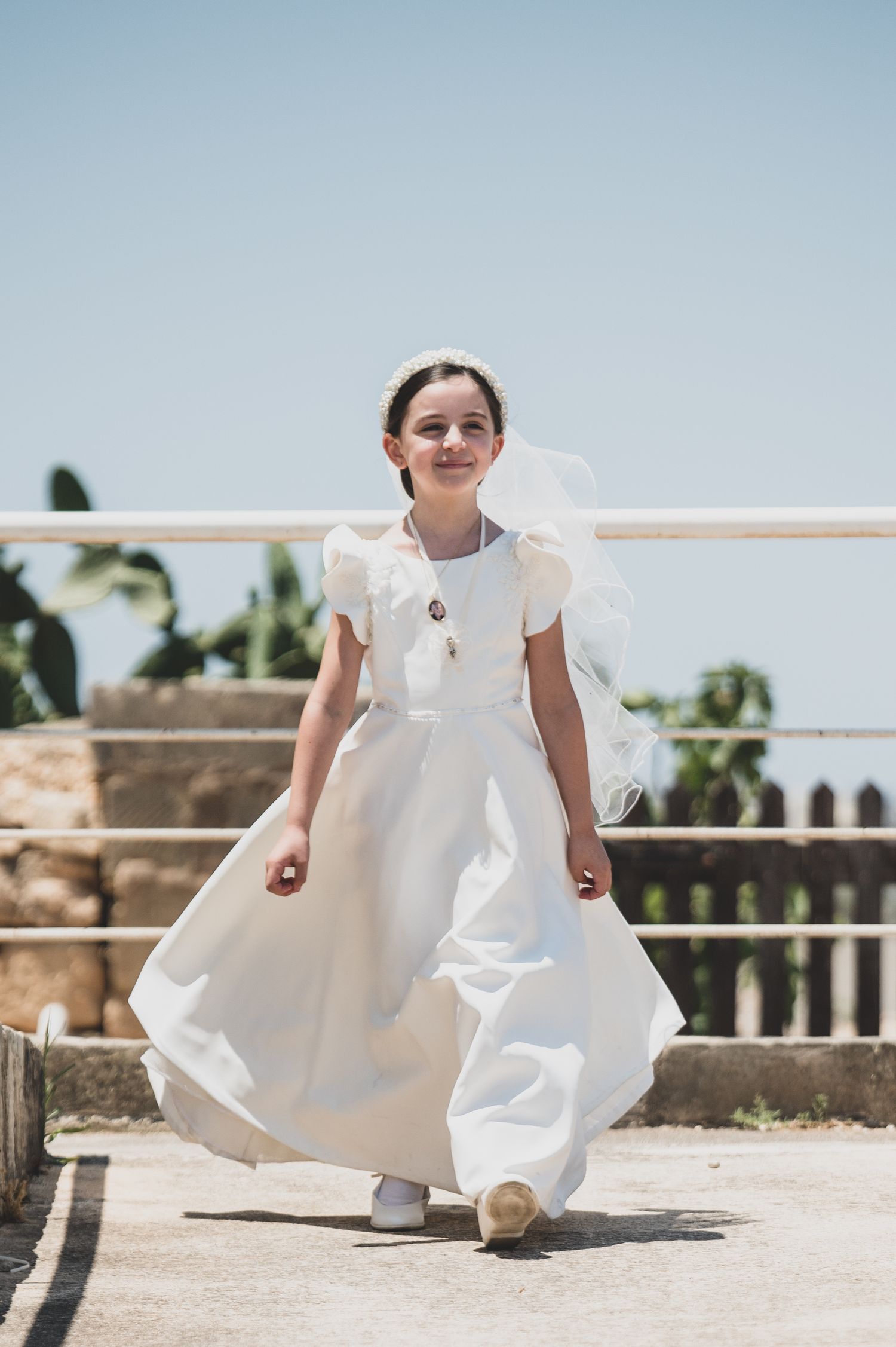 A person in a white dress poses playfully on a sunny outdoor terrace.