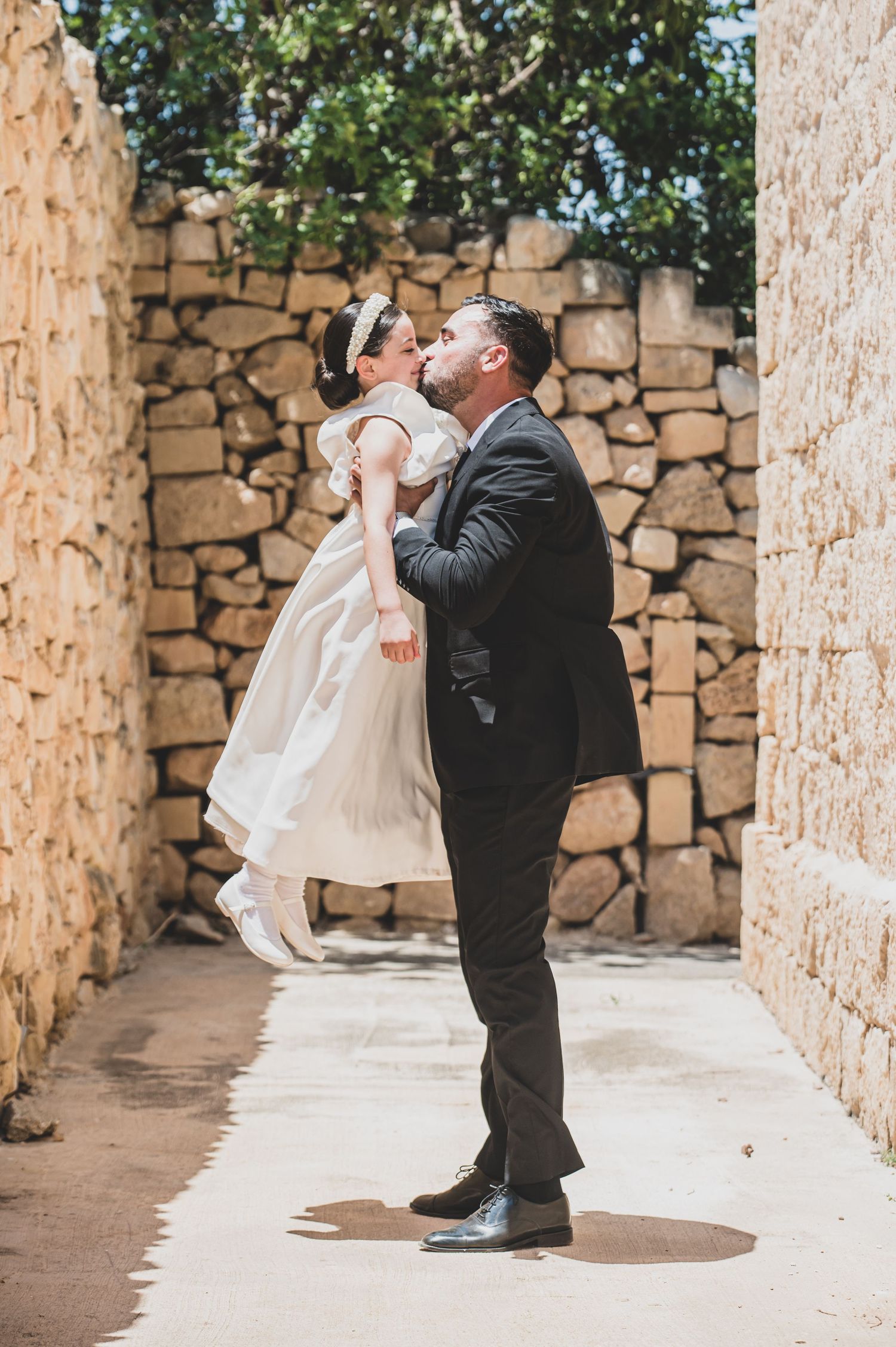 A photographer in black suit captures photos of a white dress in a stone-walled courtyard.