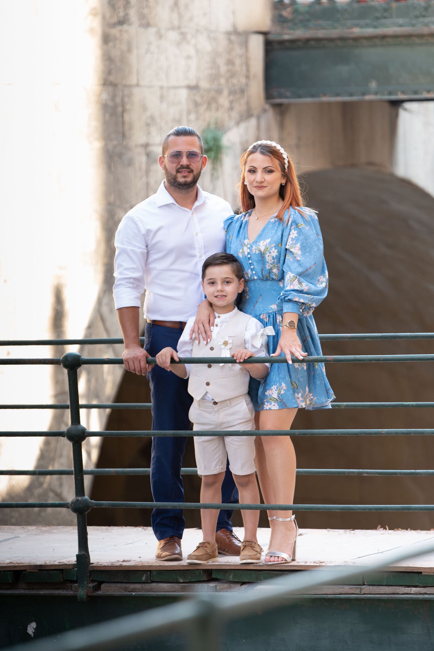 Family standing together on a balcony with metal railings in coordinated outfits.