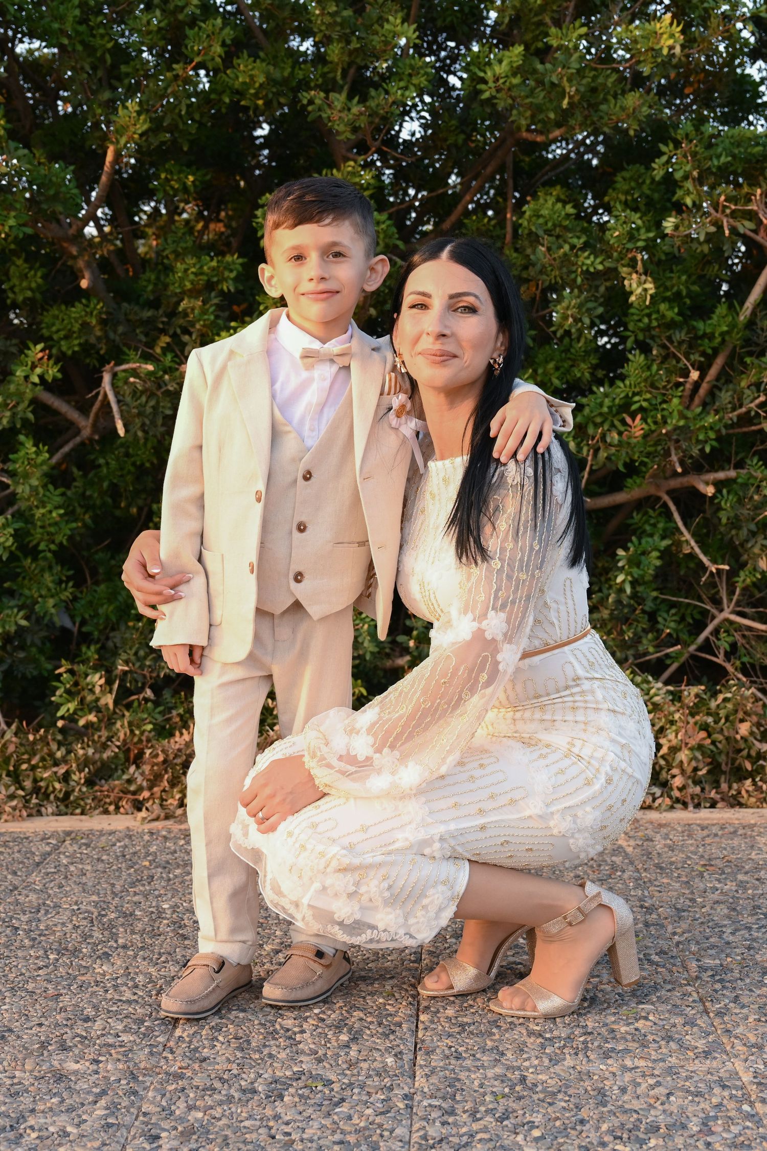 Outdoor family portrait in cream colored formal wear against green foliage.