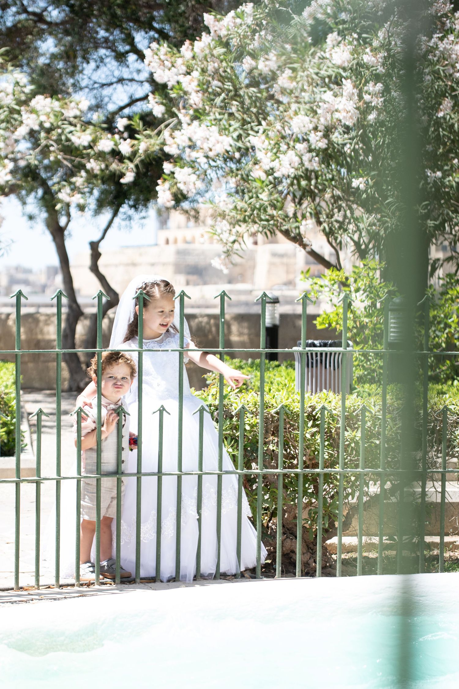 A white dress photographed through blooming spring trees and garden railings.
