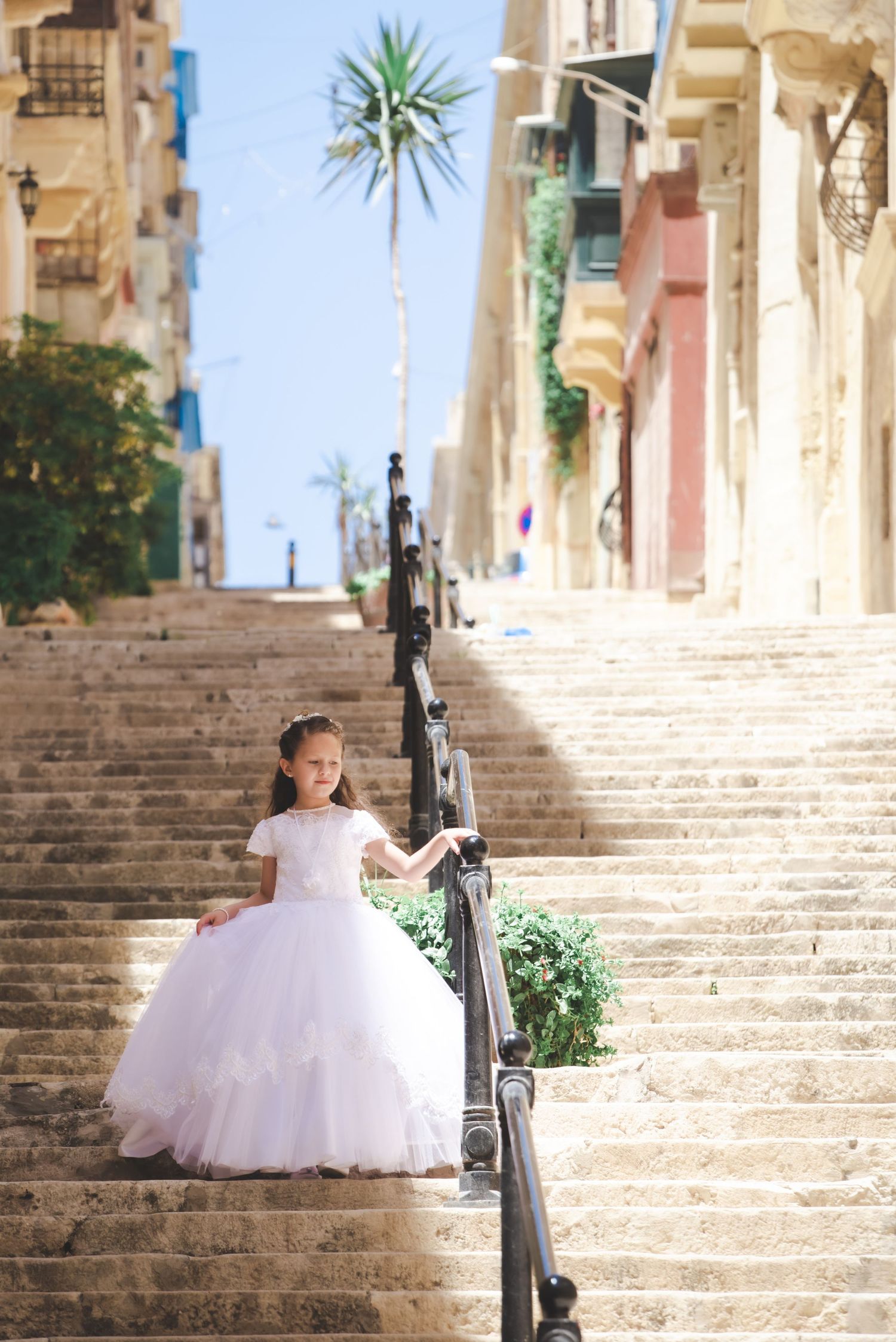 A puffy white dress photographed on sunny Mediterranean stone steps with palm trees in the background.