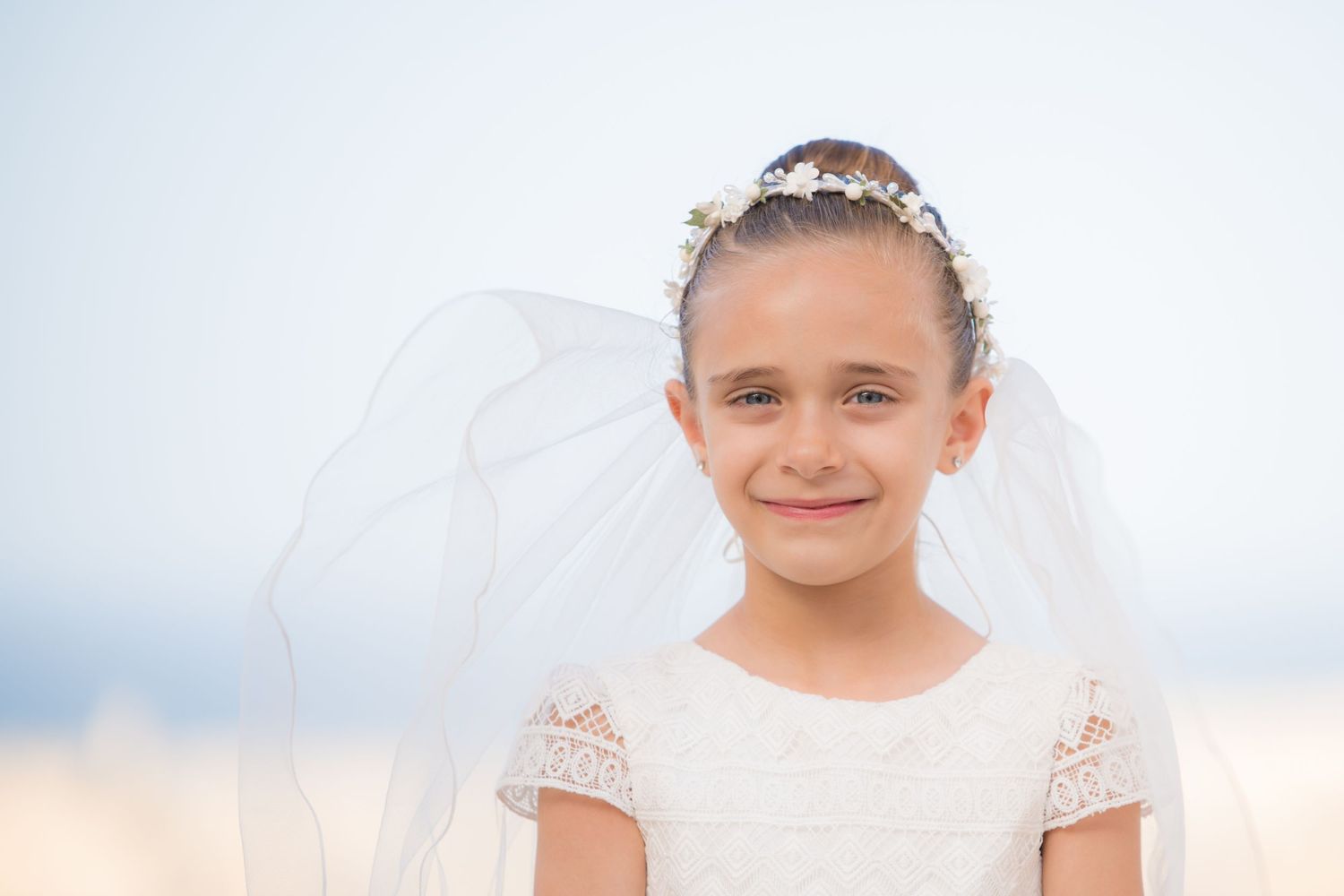A young child in a white dress with lace details poses against a bright background.
