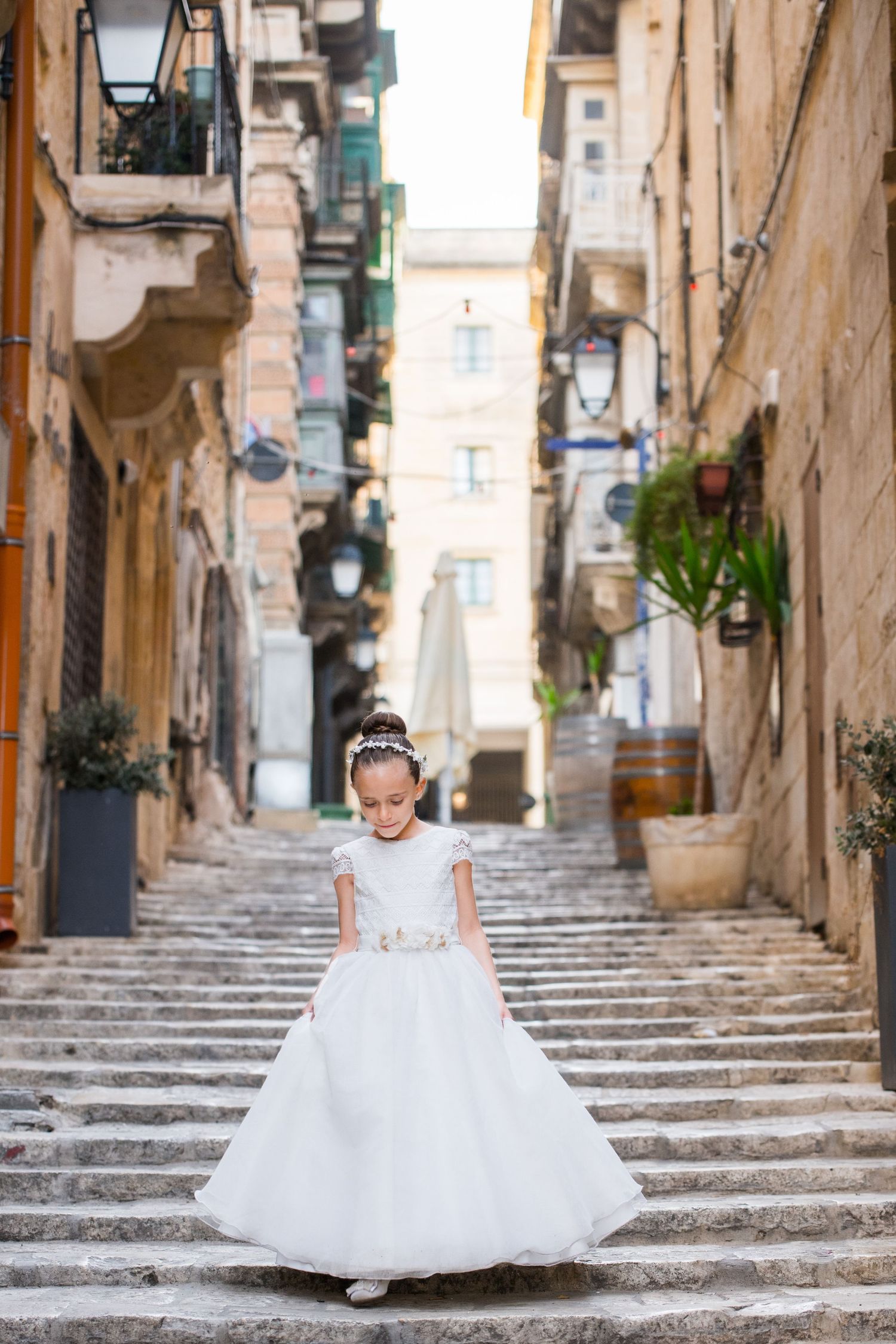 A flowing white dress descends ancient stone steps in a picturesque Mediterranean alleyway.