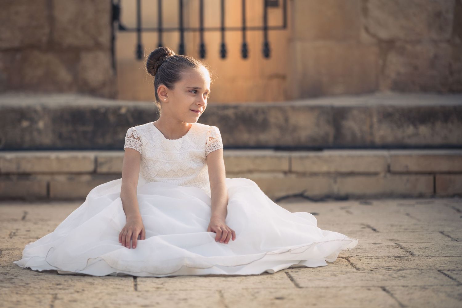 Elegant white dress spreads across weathered stone pavement in warm sunlight.