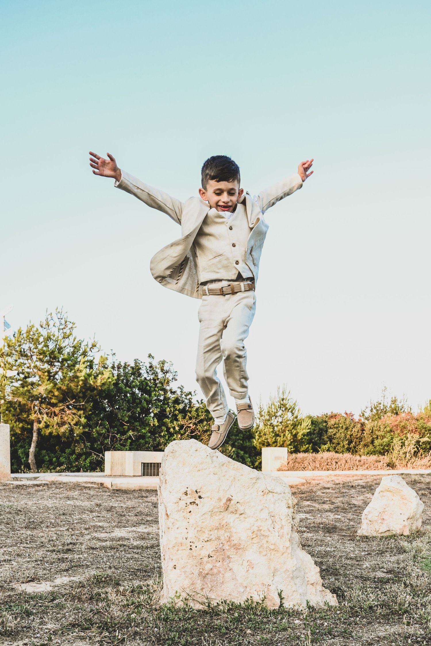 A person in beige clothing performs a dynamic jump sequence over a stone block in an outdoor setting.