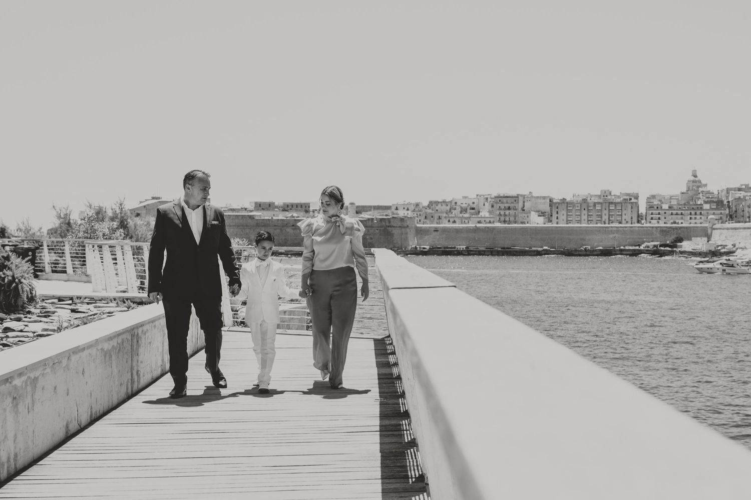 Three people walking together along a waterfront boardwalk in black and white.