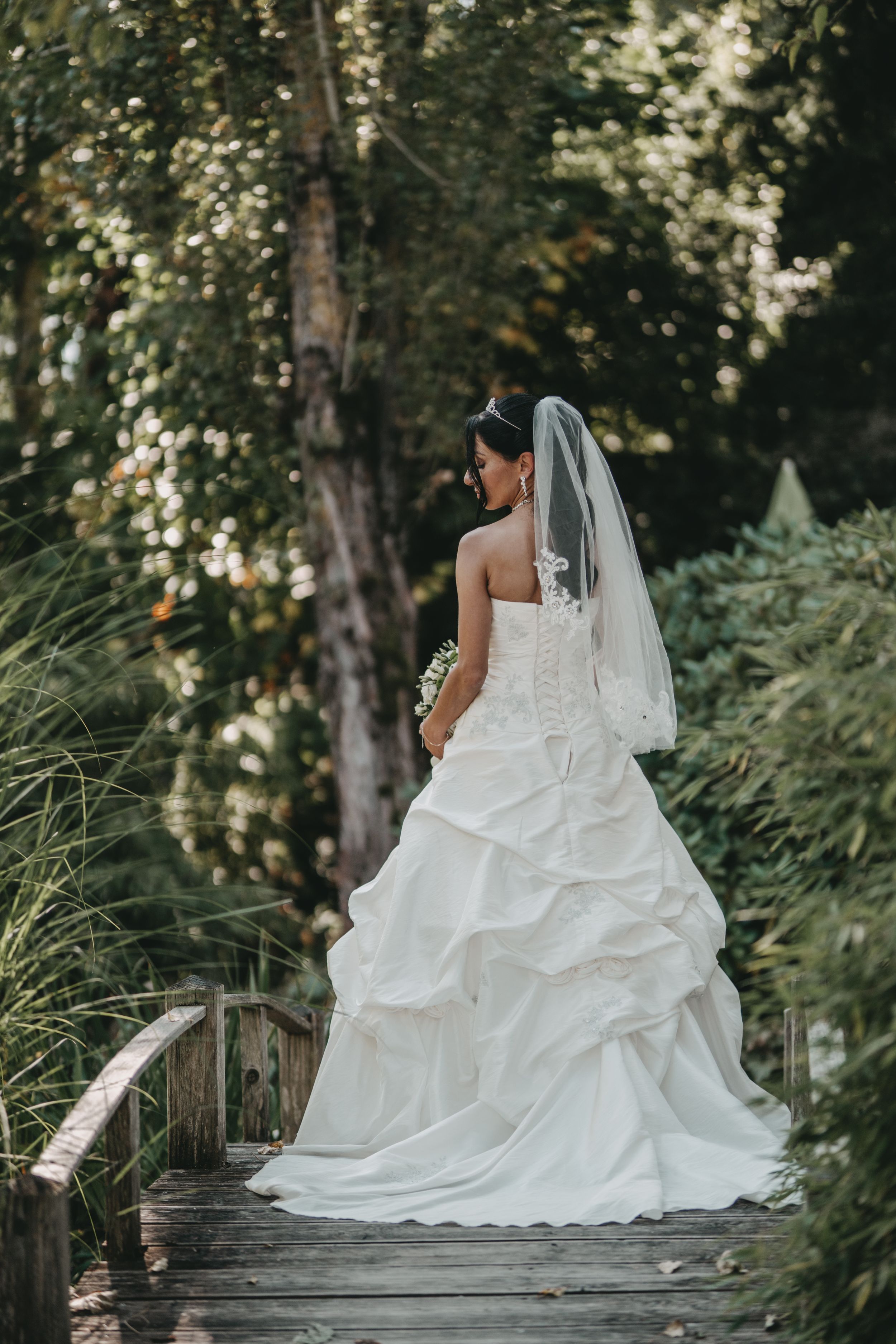 Dramatic bridal portrait showing full wedding gown against natural outdoor backdrop.