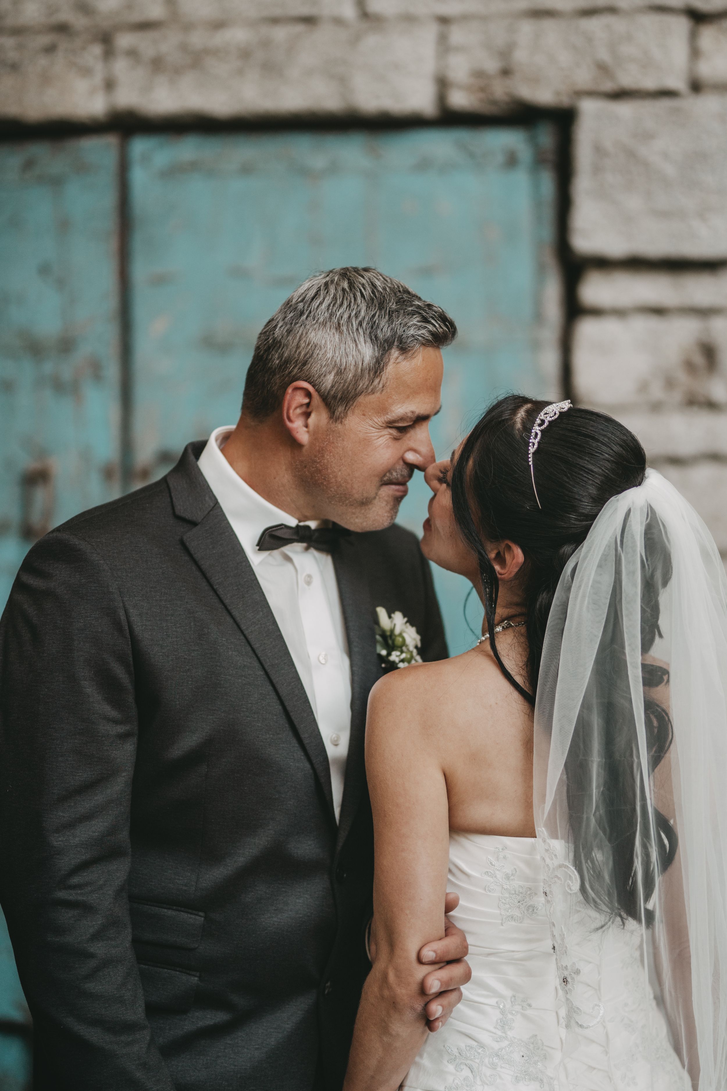 Intimate wedding portrait against rustic stone and turquoise wall background.